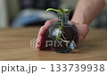 Male hand turns small vase with a sprout with long roots in water.  133739938