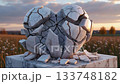 A large marble heart sculpture sits cracked on a pedestal in an open field. The sun sets in the background, casting a warm glow and highlighting the fractures in the sculpture. 133748182
