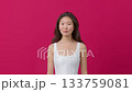 Confident young woman in white top smiling against pink studio background.  133759081