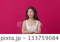 Pondering young woman in white dress standing against bold pink background.  133759084