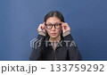 Confident young woman in black blazer and glasses against blue background.  133759292