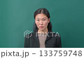 Portrait of serious young woman in black blazer on green background.  133759748