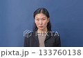Portrait of young woman in black blazer posing against solid blue background.  133760138