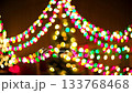 A soft, blurred view of multicolored string lights from a garland and a Christmas tree, with the camera smoothly zooming out to reveal more of the festive, abstract holiday scene 133768468