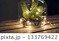Twinkling fairy lights encircle evergreen in glass cloche on wooden table 133769422