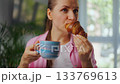 Woman enjoying a fresh croissant and coffee for breakfast. 133769613