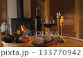 Slow living scene with wine, bread and candles by fireplace. Cozy interior 133770942