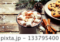 Hot chocolate with marshmallows in an enamel mug on a wooden table, surrounded by cinnamon sticks, cookies, pine branches and soft winter decorations cozy Christmas and winter holiday food 133795400