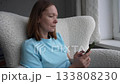 Engaging moments of a woman using her phone while relaxing in a cozy chair at home during the afternoon 133808230