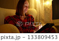 A person sits comfortably on a couch, sketching on a tablet. The warm light from string decorations creates a cozy atmosphere for creativity at night. 133809453