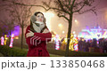 A young beautiful girl in a red coat walks in the evening at the European Christmas Market against the backdrop of illuminations and garlands. 133850468
