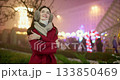 A young beautiful girl in a red coat walks in the evening at the European Christmas Market against the backdrop of illuminations and garlands. 133850469