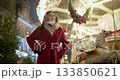 A young beautiful girl in a red coat walks in the evening at the European Christmas Market against the backdrop of a festive carousel with illuminations. 133850621