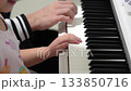 A young girl and a man play piano side-by-side during daytime. They are making lovely music together, with small hands learning from a bigger set. Practice makes perfect. 133850716