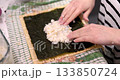 Someone is carefully spreading cooked sushi rice on a sheet of nori seaweed, placed on a bamboo mat. They are making sushi at home 133850724