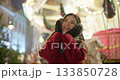 A young beautiful girl in a red coat walks in the evening at the European Christmas Market against the backdrop of a festive carousel with illuminations. 133850728