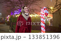 A young beautiful girl in a red coat walks in the evening at the European Christmas Market against the backdrop of illuminations and garlands. 133851396