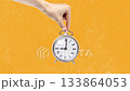 Hand holding a vintage alarm clock against a bright orange background in a creative time-themed presentation 133864053