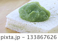 A close-up shows a wooden spoon spreading pandan custard onto soft white bread 133867626