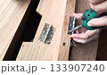 Craftsman attaching hinges to wooden structure with power screwdriver. Focus on skill, repair, and DIY home improvement. Perfect for home repair, construction and projects. 133907240
