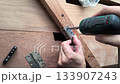 Closeup of hands attaching a metal hinge to wood using a power screwdriver. Represents DIY, repair, home improvement, construction, or craftsmanship. 133907243