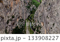 Majestic aerial view looking down into a narrow, rocky canyon. A winding river flows at the bottom alongside a scenic hiking trail 133908227