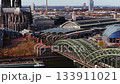 Panoramic aerial view of Cologne showing Cathedral, Hohenzollern Bridge, and central train station with trains arriving and departing 133911021