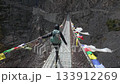 Wide Shot Back View of a hiker crossing a suspension bridge in rugged, high-altitude mountains. Prayer flags add cultural and adventure context. Nepal, Annapurna circuit trek. 133912269