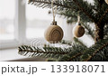 Close-up of a simple wooden Christmas ornament with visible grain, hanging on a pine tree branch by a window. Minimalist Scandinavian decor in soft natural light creating a cozy, eco-friendly holiday 133918071