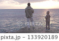 A father and son fish together by the sea at sunset, sharing a peaceful moment by the water. Dressed 133920189