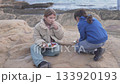 Two young girls are sitting on rocky seaside cliffs, enjoying a simple outdoor meal together.  133920193