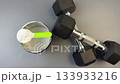 Fitness supplement container features a green scoop and black dumbbells, highlighting the workout essentials, camera pans and zooms in for emphasis 133933216
