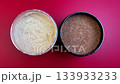 Close-up view of two different exfoliating scrubs, one creamy and one granular, on a bright red background, emphasizing texture and visual contrast as camera zooms in 133933233