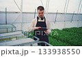 Agricultural technology. Using an electronic device, a farmer takes a sample from a plant watering container and measures the water's acidity and pH levels. Growing flowers and tulips in a greenhouse. 133938550