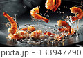 Succulent shrimps falling into sizzling hot oil within professional kitchen wok, generating dynamic oil splashes and droplets against pristine black background during precise cooking process 133947290