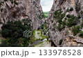 Stunning aerial perspective flying backward out of a narrow, steep walled canyon with a river flowing below, gradually revealing a vast, green forest 133978528
