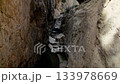 High angle view slowly panning down into a deep and narrow rocky gorge. A small mountain stream with waterfalls flows over large boulders 133978669