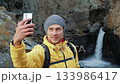 Hiker taking a selfie with his phone at a waterfall 133986417