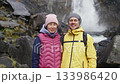 Asian woman, caucasian man stands together near waterfall 133986420