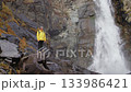 Hiker admiring powerful waterfall in rocky mountains 133986421