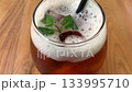 cold iced tea in a rounded glass, topped with foam and fresh mint, with a black straw. Inviting and casual, perfect for summer cafe or lifestyle imagery, Refreshing Iced Tea Glass With Mint Garnish An 133995710