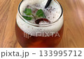 cold iced tea in a rounded glass, topped with foam and fresh mint, with a black straw. Inviting and casual, perfect for summer cafe or lifestyle imagery, Refreshing Iced Tea Glass With Mint Garnish An 133995712