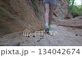 Woman in shorts trekking through a deeply cut, shaded earthen gorge. Low angle emphasizes scale. 134042674