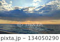 Seascape. Dark rainy clouds in blue orange sky over sea. Sunbeams from behind clouds. Sea waves on sand of seashore on sunset sunrise. Yellow reflection of sunlight on surface of sea waves. 134050290