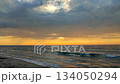 Sea waves with blue water on sand of seashore on sunset and sunrise. Yellow reflection of sunlight on surface of sea waves. Orange sky with dark rain clouds, horizon line and sea waves on sand. 134050294
