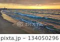 Sea waves with blue transparent water on sand of seashore on sunset and sunrise. Yellow reflection of sunlight on surface of sea waves. Sky with dark rain clouds, horizon line and sea waves on sand. 134050296