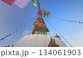 Low Angle Shot of the historic Swayambhunath Stupa against a blue sky. Colorful prayer flags frame the golden spire. Cultural travel concept. 134061903
