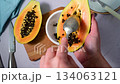 Female hands taking off the seeds from Papaya orange fruit, bright background 134063121