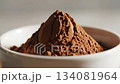 A perfectly sculpted mound of rich dark brown cocoa powder rests in a simple white bowl, highlighting its fine texture and deep color, ready for baking or beverage preparation. 134081964
