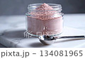 A clear glass jar filled with pale pink collagen powder sits next to a silver spoon on a pristine white marble surface, highlighting beauty and wellness concepts. 134081965